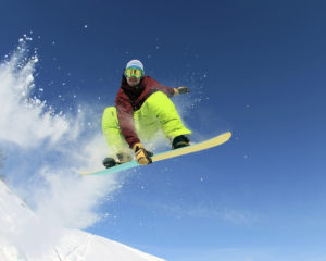 Jumping snowboarder keeps one hand on the snowboard on blue sky background